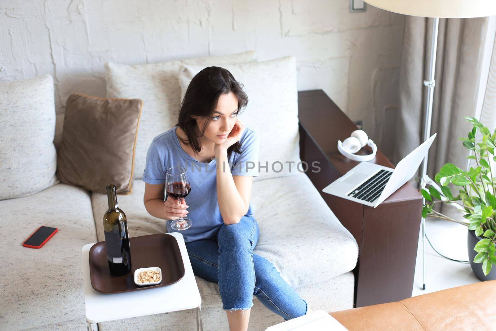 Successful young beautiful woman sitting on a sofa in the living room, drinking red wine