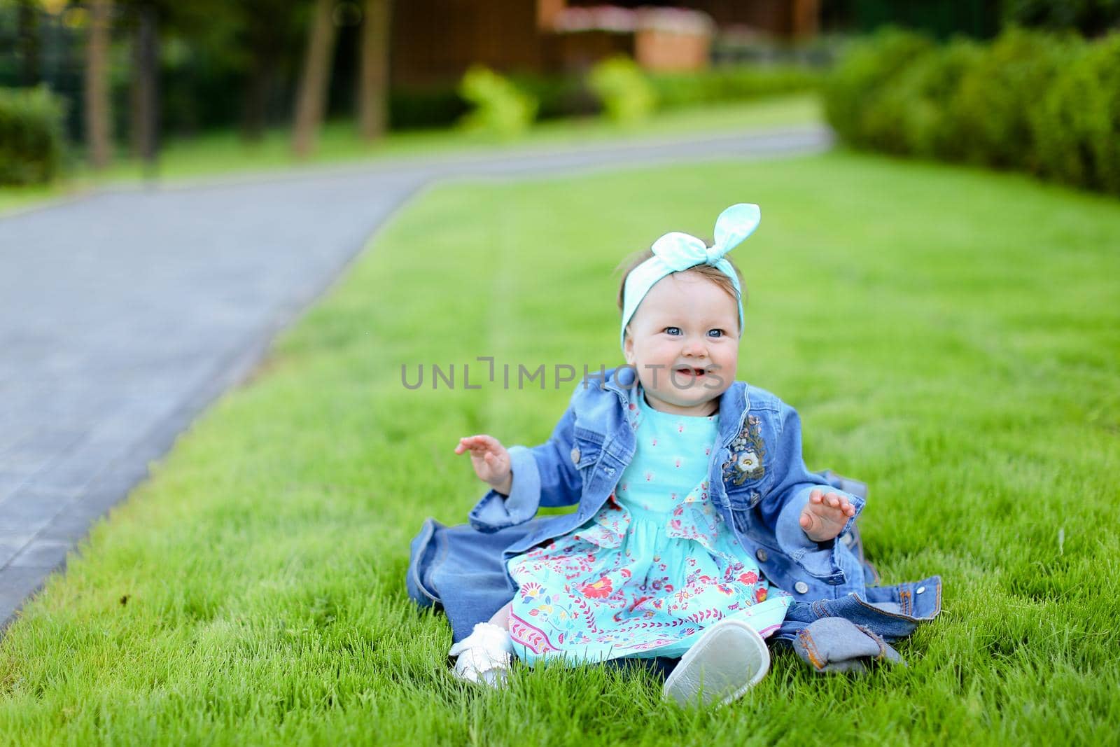 Little cute female child sitting on green grass and wearing jeans jacket. by sisterspro