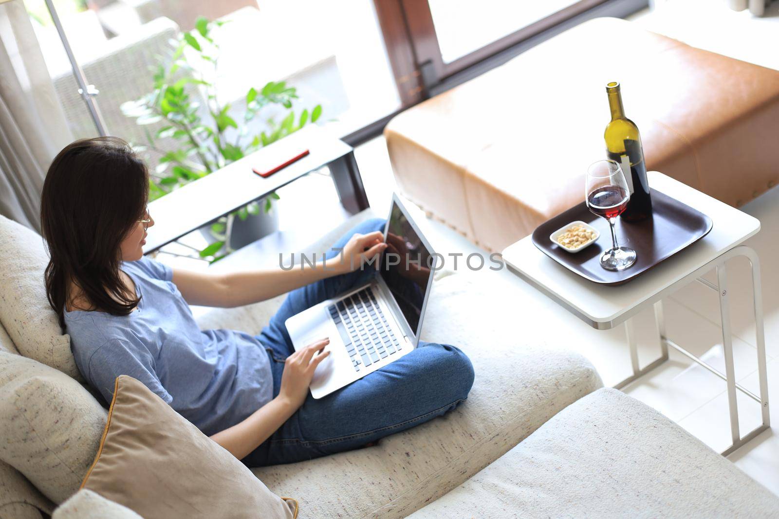 Smiling young woman sitting on sofa with laptop computer and chating with friends. Top view