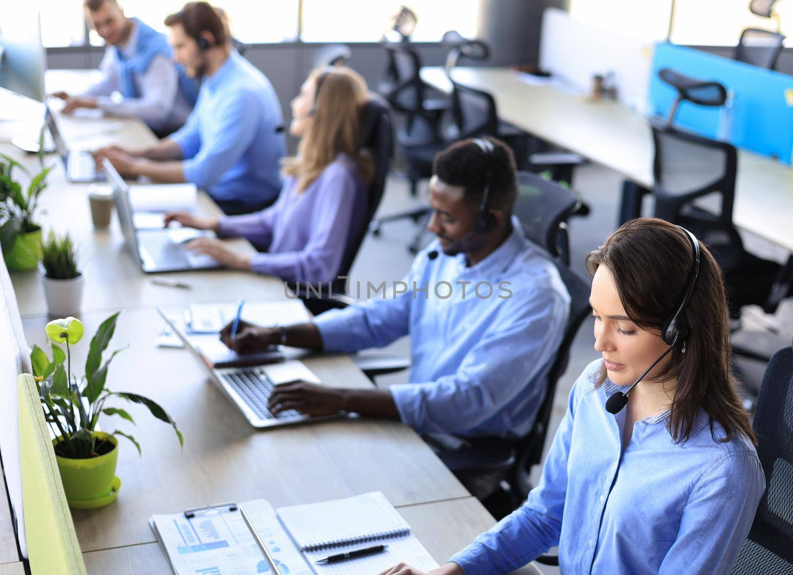 Female customer support operator with headset and smiling, with collegues at background