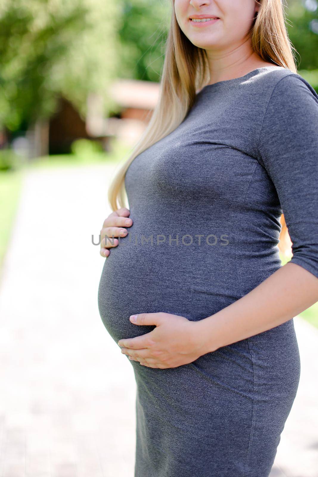 Young blonde pregnant woman wearing grey dress holding belly. by sisterspro