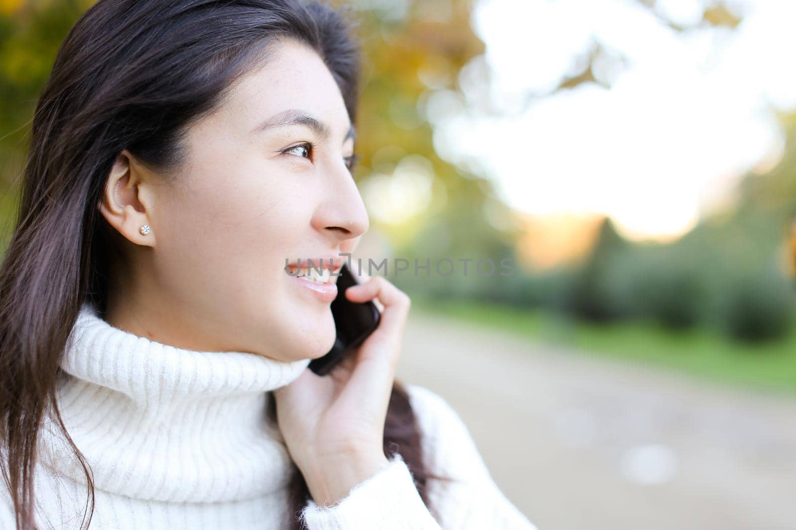 Close up asian smling girl wearing white sweater talking by smartphone and walking in park. by sisterspro