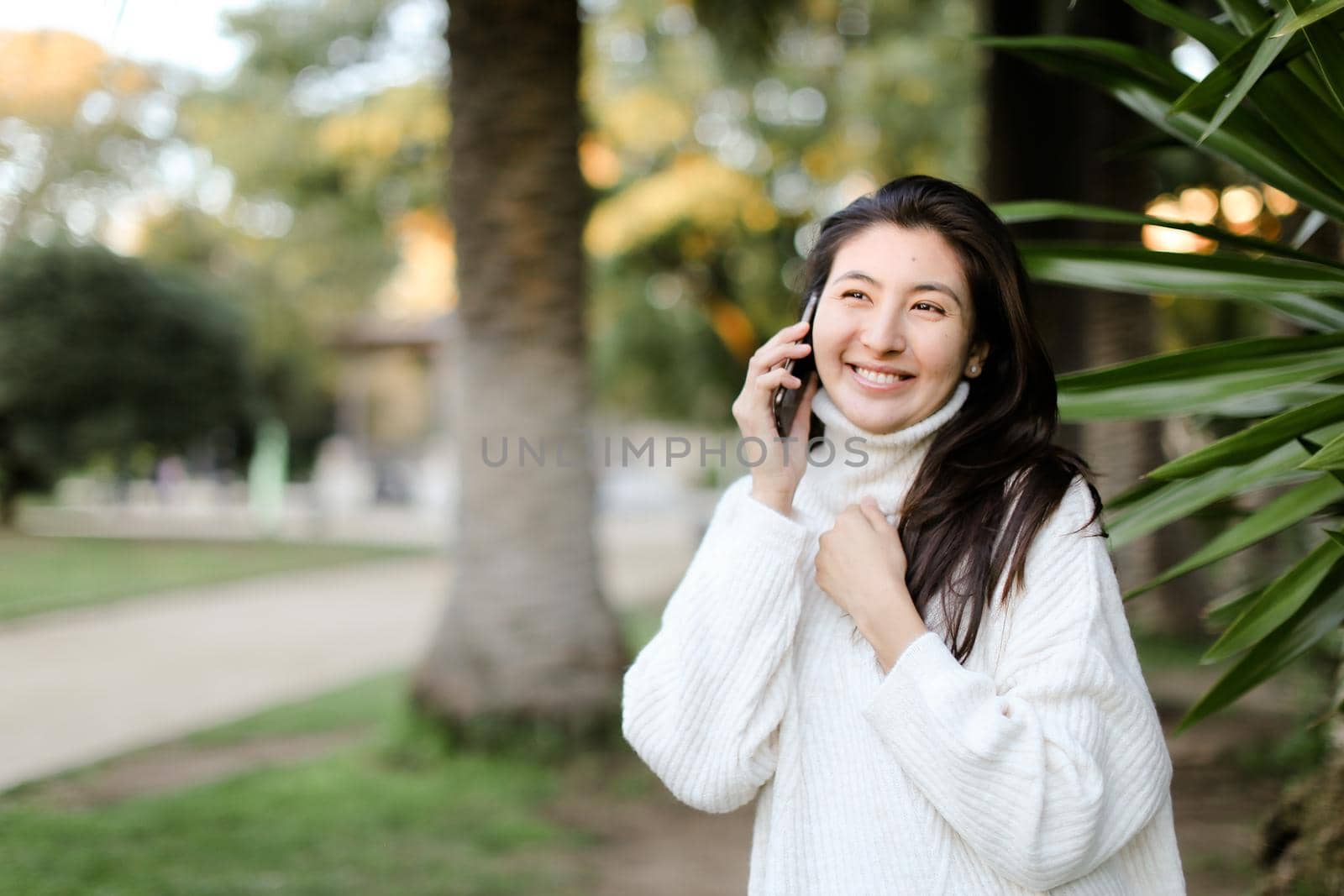 Japanese girl in tropical park talking by smartphone near palm. by sisterspro