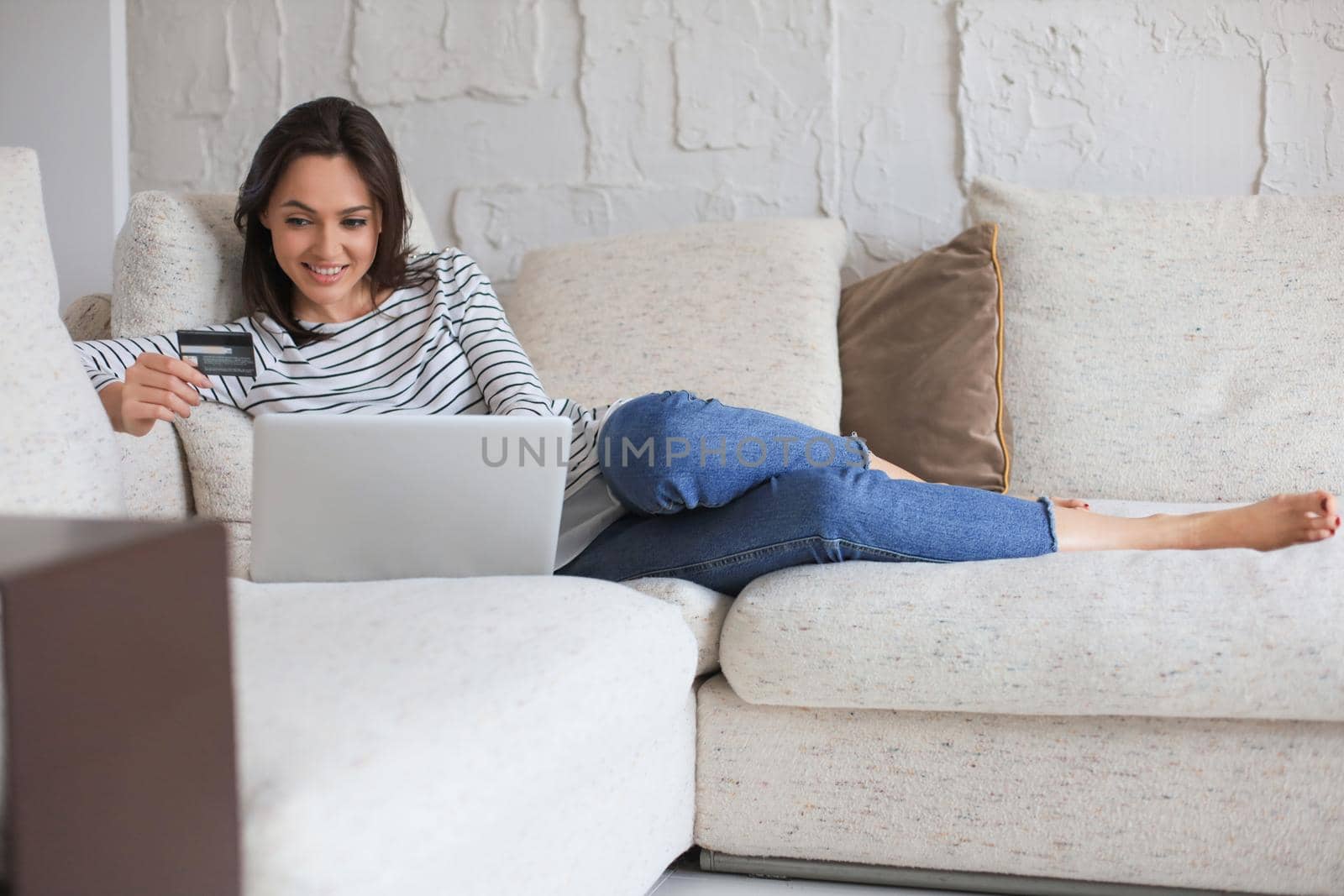 Happy natural brunette using credit card and laptop in the living room. by tsyhun
