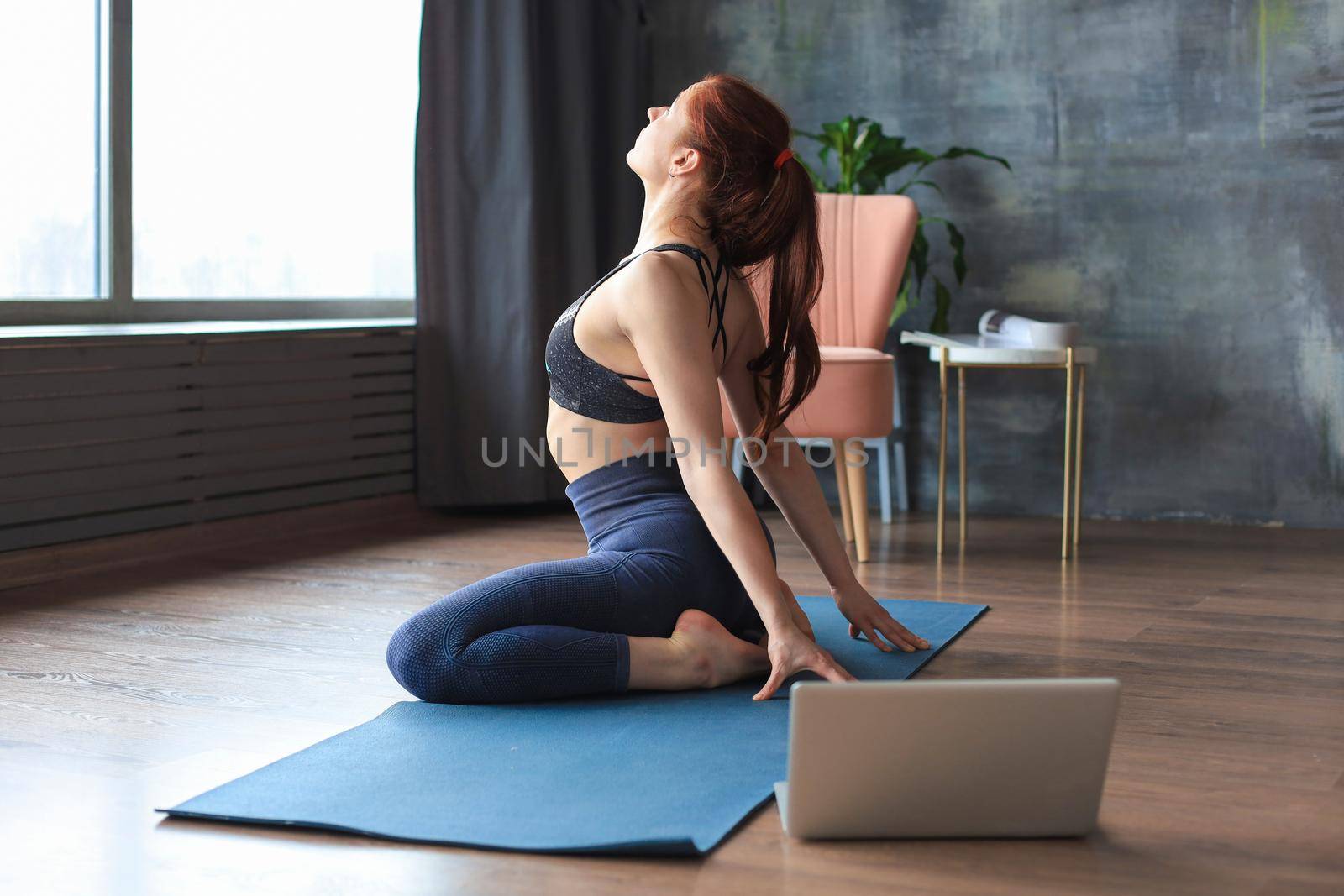 Sporty slim woman practicing advanced yoga in front of laptop, watching online tutorials. Healthy lifestyle