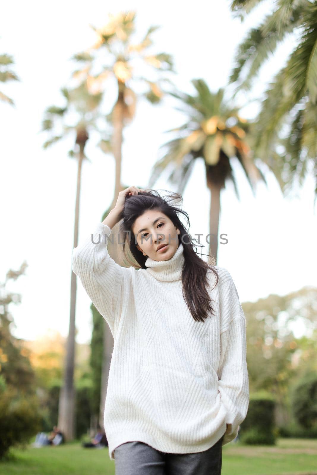 Korean nice woman walking in tropical park and wearing white sweater. Concept of nature and female person.