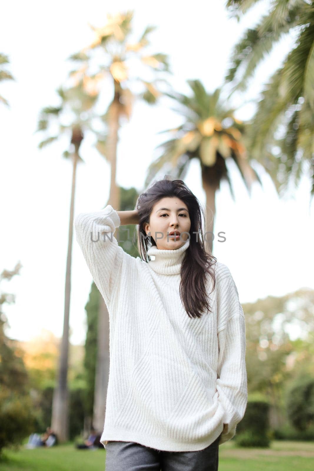 Korean cute woman walking in tropical park and wearing white sweater. Concept of nature and female person.