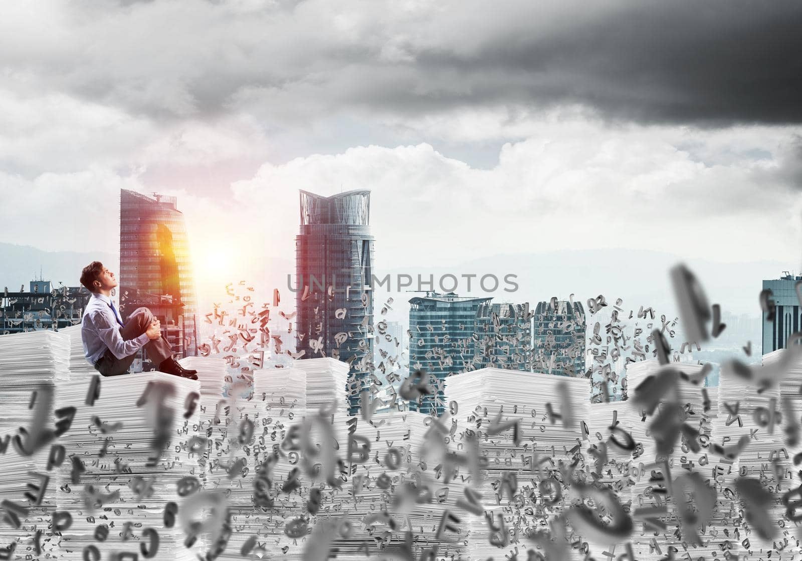 Thoughtful businessman looking away while sitting among flying letters with cityscape and sunlight on background. Mixed media.
