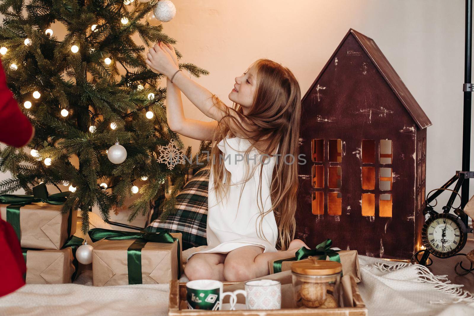 Excited girl smiling while sitting on a carpet and putting decorations on Christmas tree