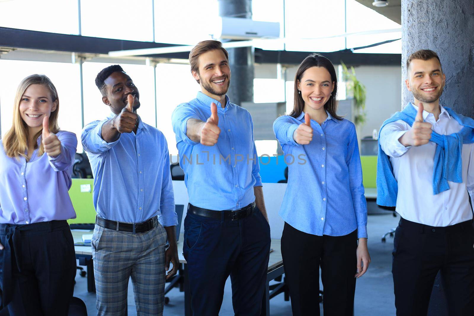 Happy businesspeople standing in office showing thumb up