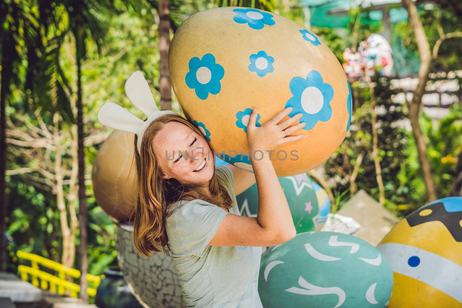 Beautiful young woman with bunny ears having fun with traditional Easter eggs hunt, outdoors. Celebrating Easter holiday.