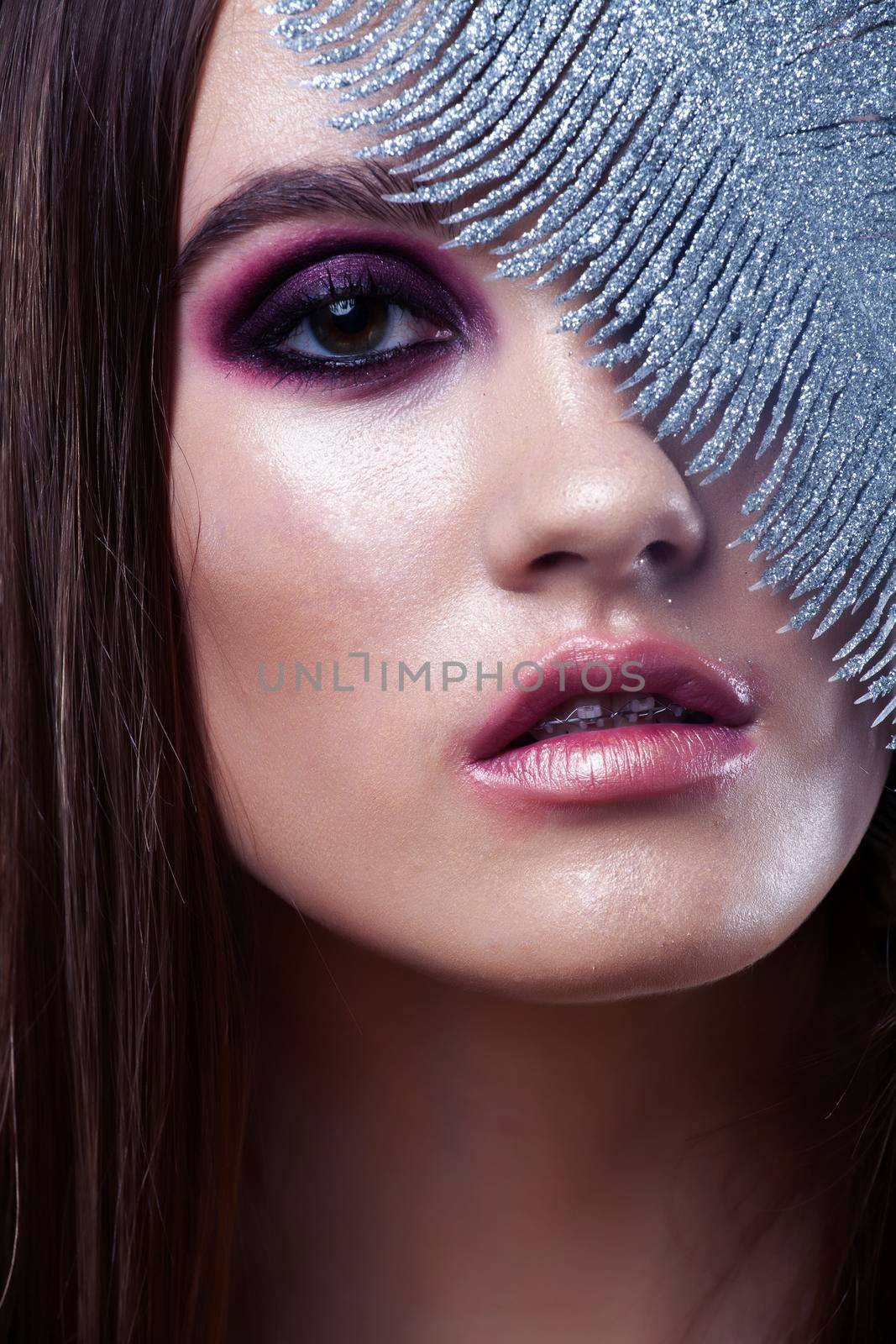 beauty brunette young girl with fashion makeup and silver feather close up on white background