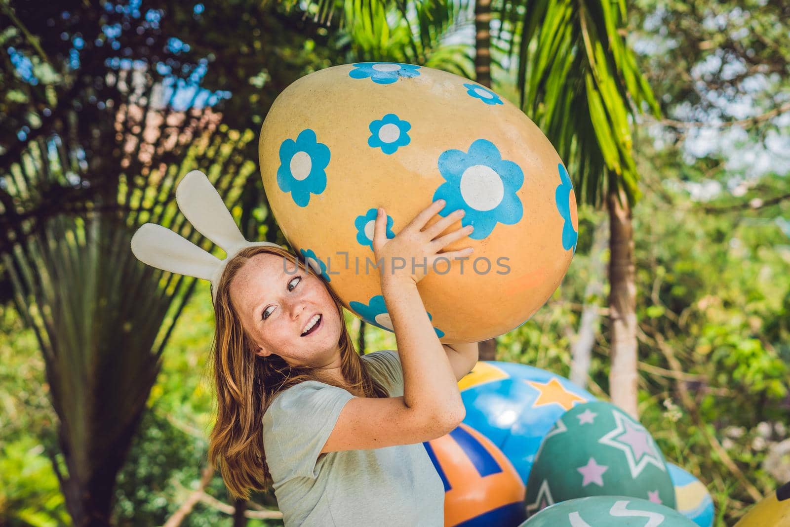 Beautiful young woman with bunny ears having fun with traditional Easter eggs hunt, outdoors. Celebrating Easter holiday by galitskaya