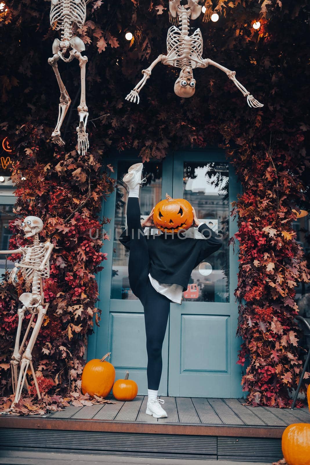 Girl with a pumpkin head posing at the door on the street . Halloween Concept