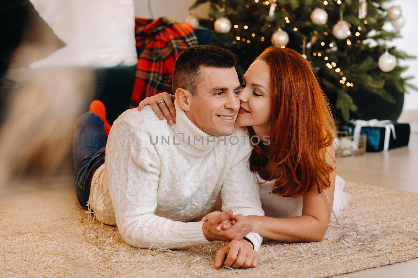 a happy married couple is lying on the floor near the Christmas tree at home.