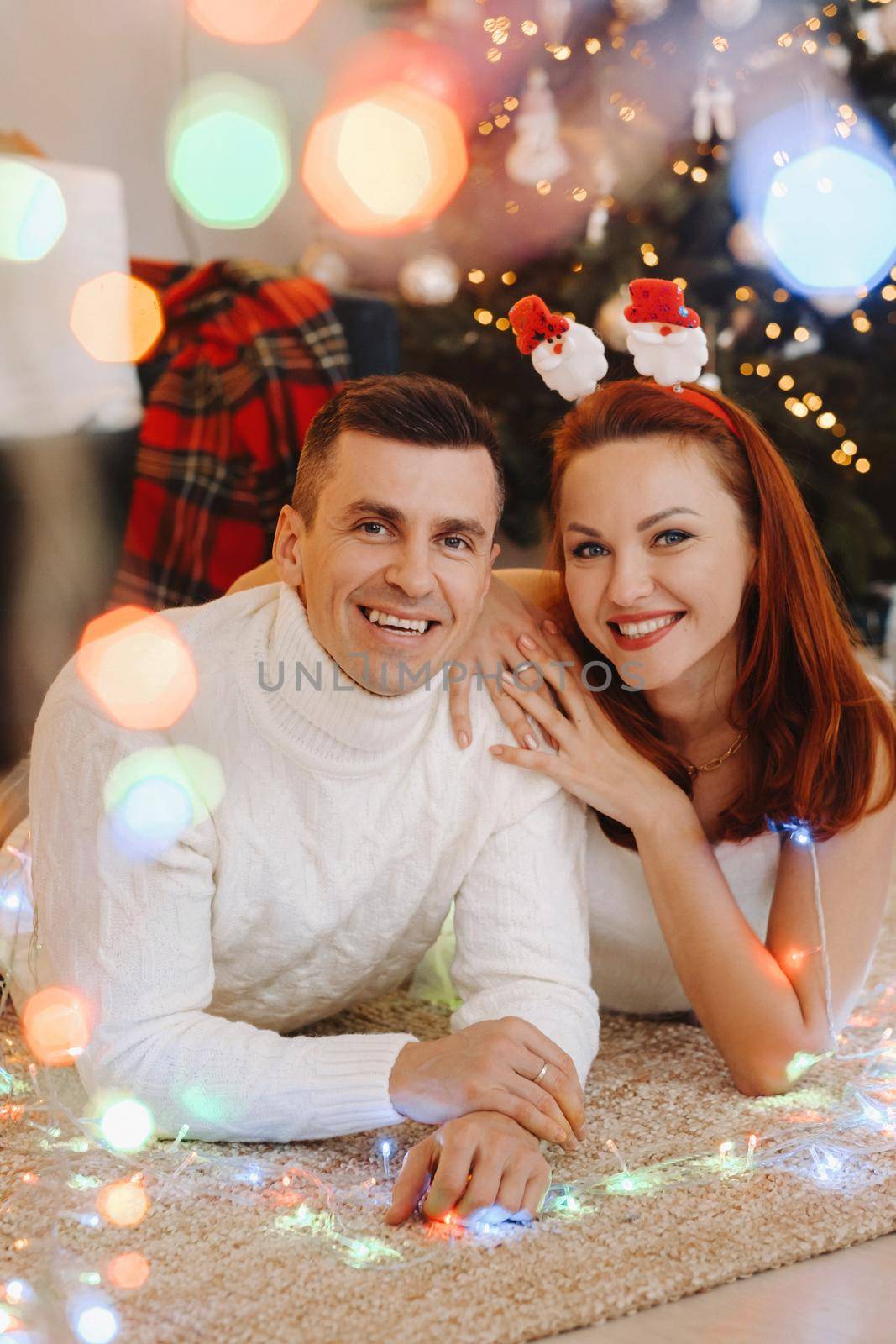 a happy married couple is lying on the floor near the Christmas tree at home.