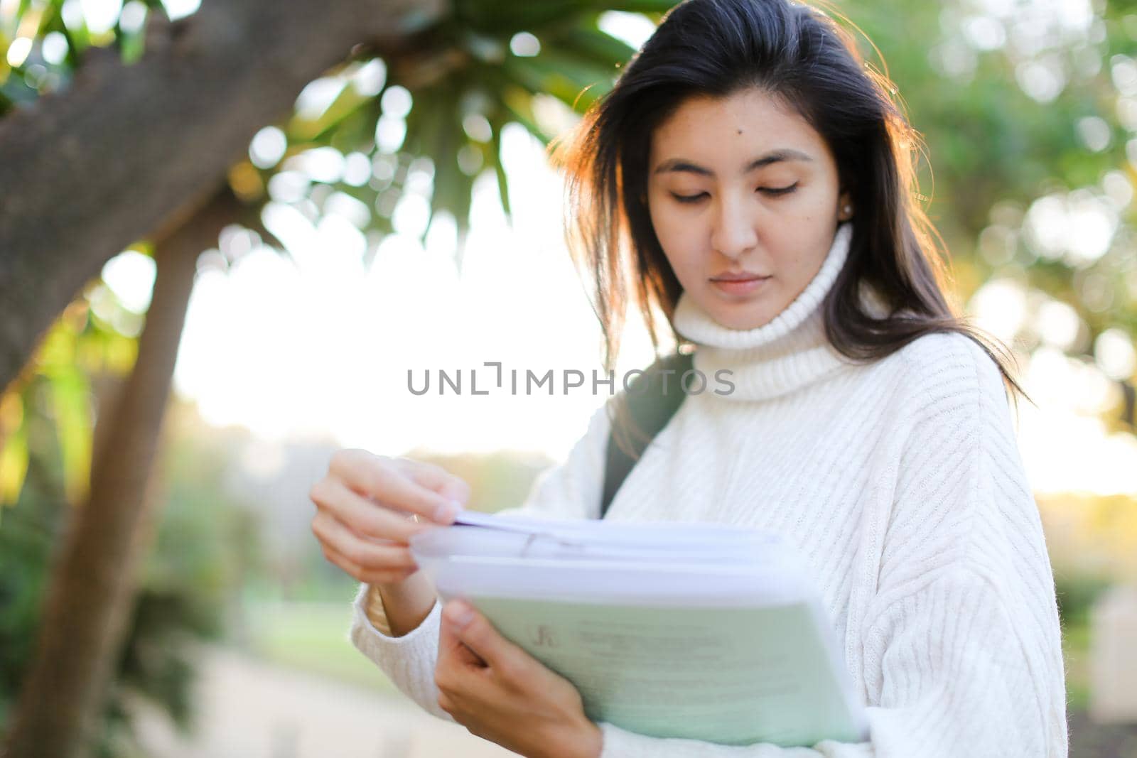 Focus on chinese girl keeping documents and walking outdoors. Concept of asian student.