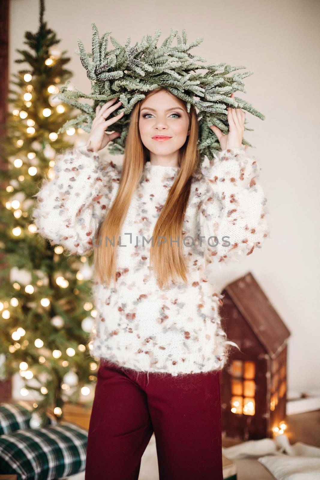 Portrait of a gorgeous young woman with long hair wearing fir Christmas wreath on head, smiling at camera.