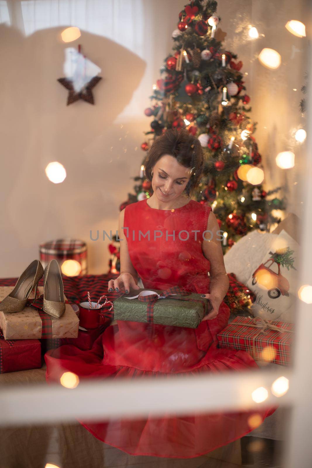 Attractive woman in red dress looks at the box with Christmas gift by StudioLucky