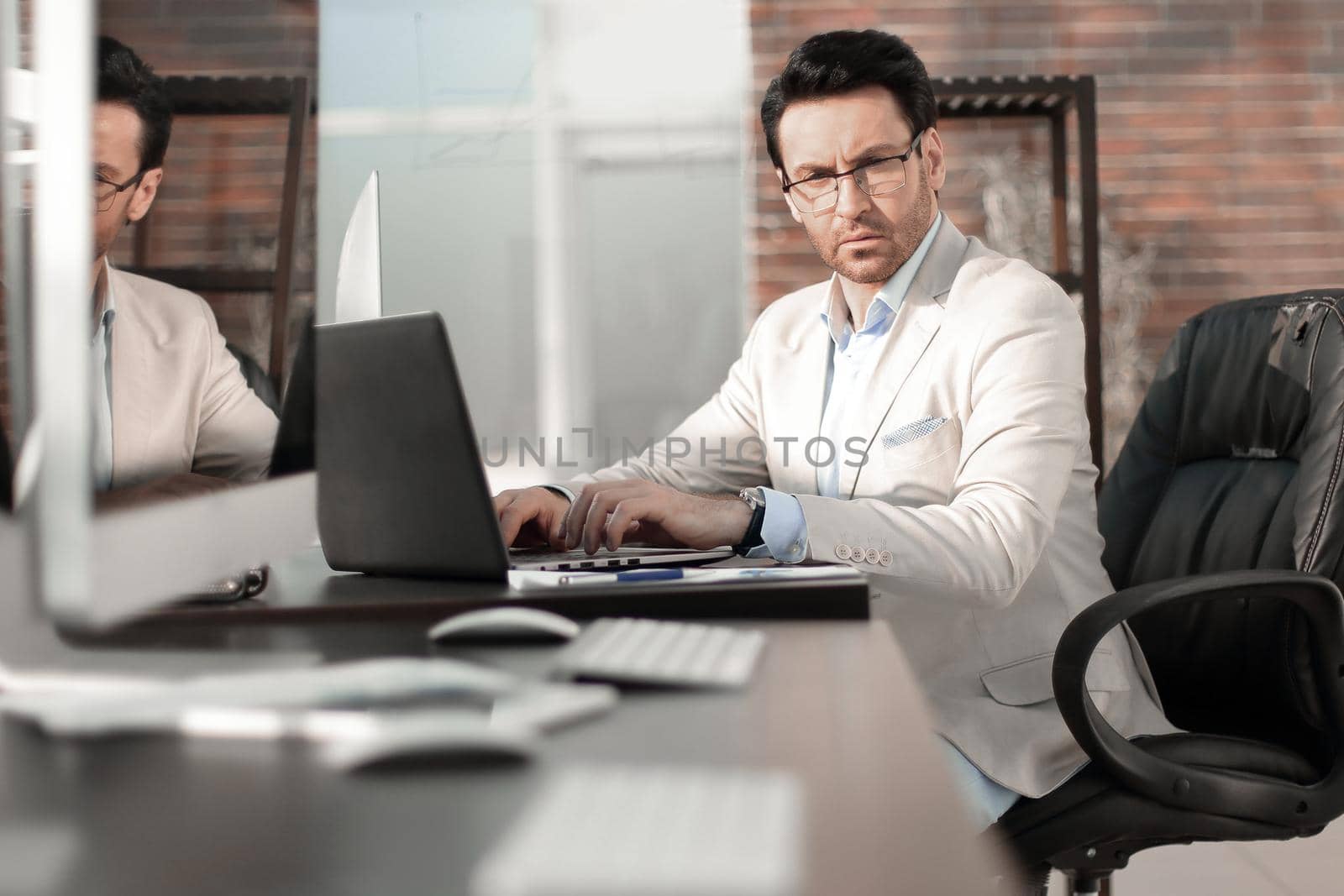 behind the glass.a serious businessman using a laptop to work in the office.business background