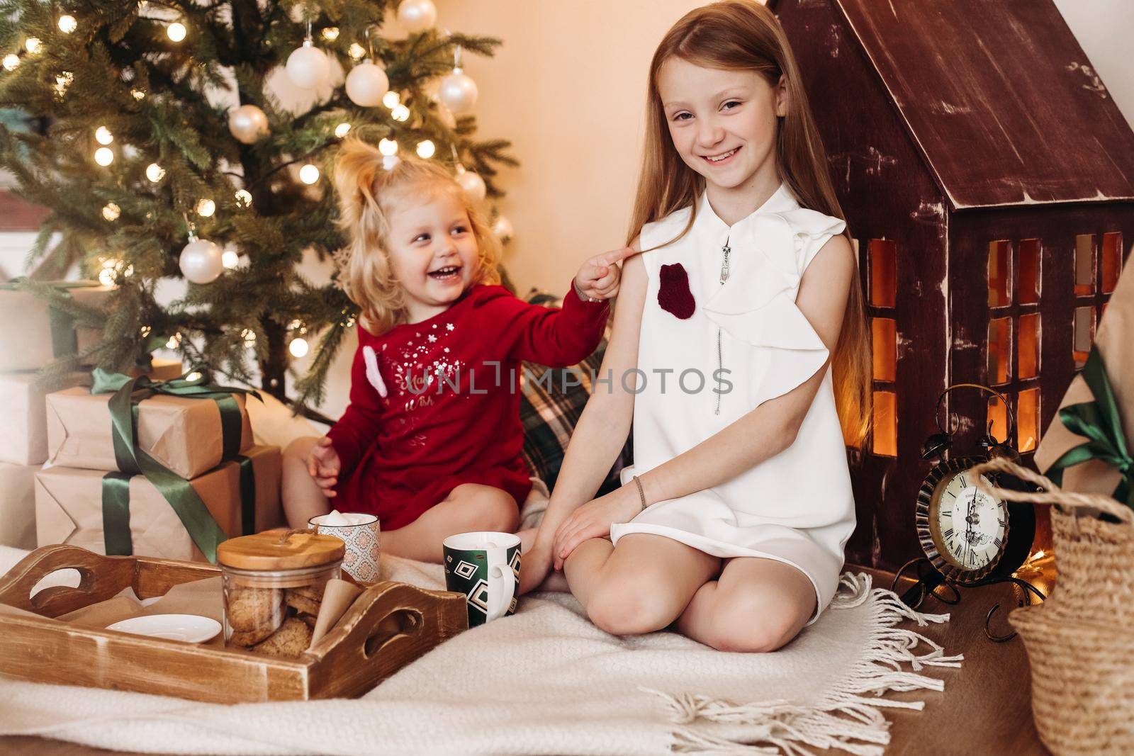 Little pretty girl sith wavy hair sits with a box with a present and rejoices with her elder sister by StudioLucky