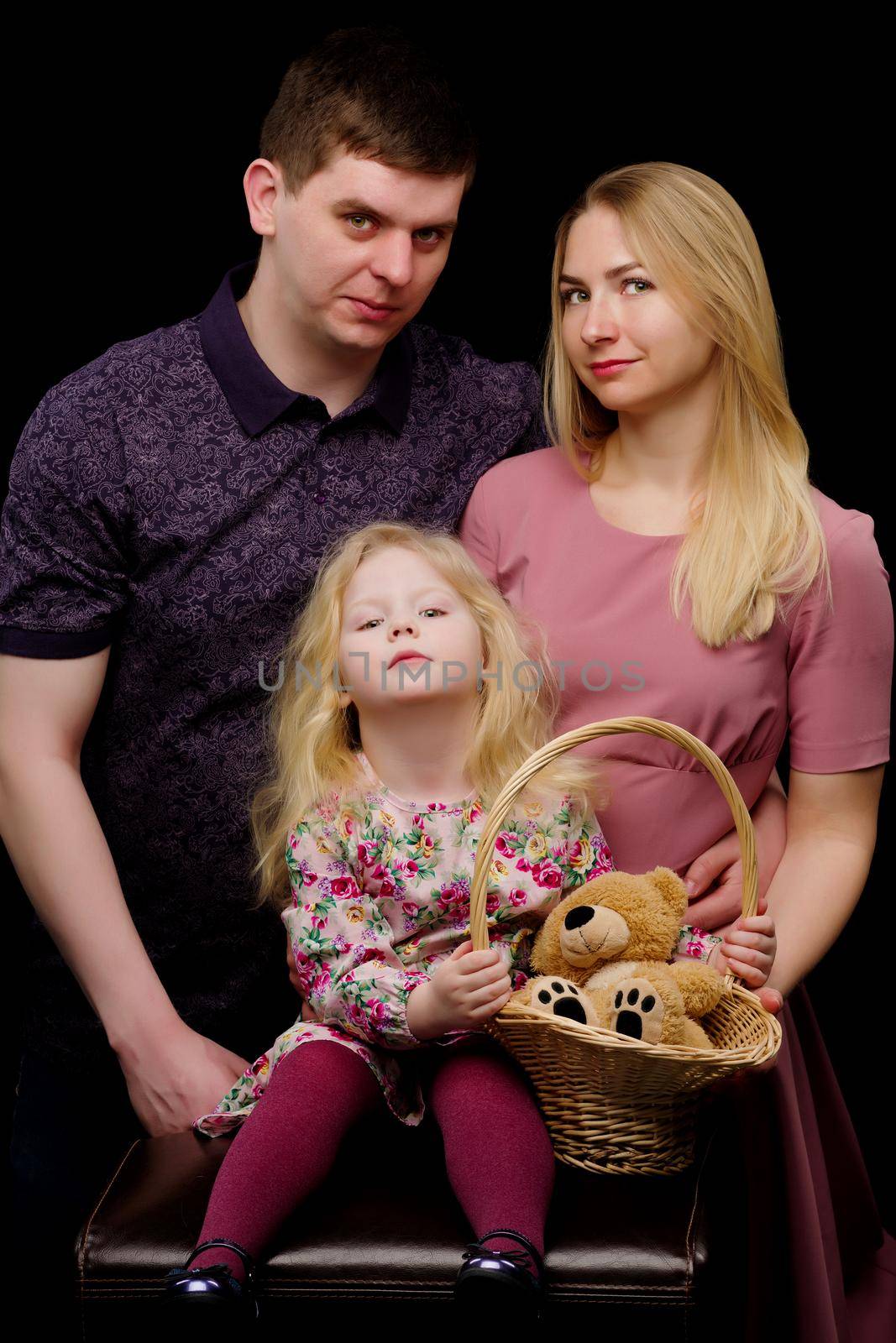 Family portrait, mom and dad with a charming little daughter. On a black background. The concept of family happiness.