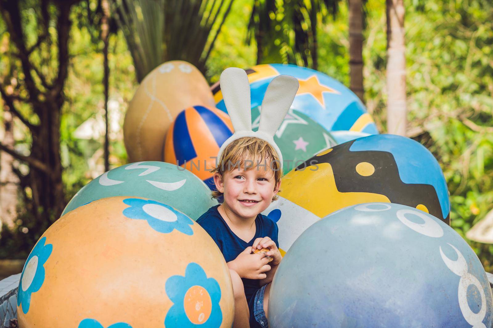 Cute little kid boy with bunny ears having fun with traditional Easter eggs hunt, outdoors. Celebrating Easter holiday. Toddler finding, colorful eggs.