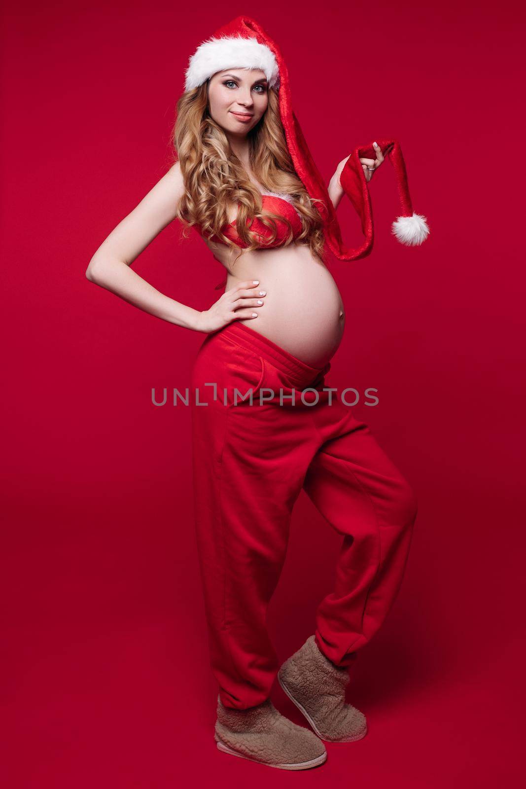 Attractive young mom with bright makeup poses for Christmas photo shoot isolated on red background