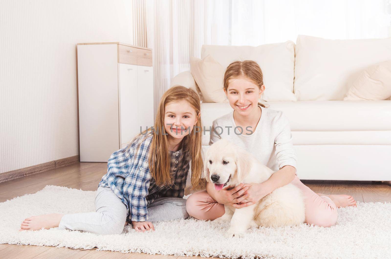 Smiling sisters sit together with retriever puppy by GekaSkr