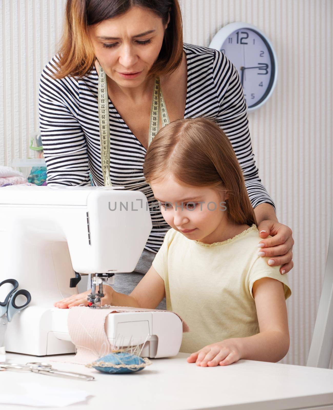 Attractive woman showing child pupil how to easy work with sewing machine at home