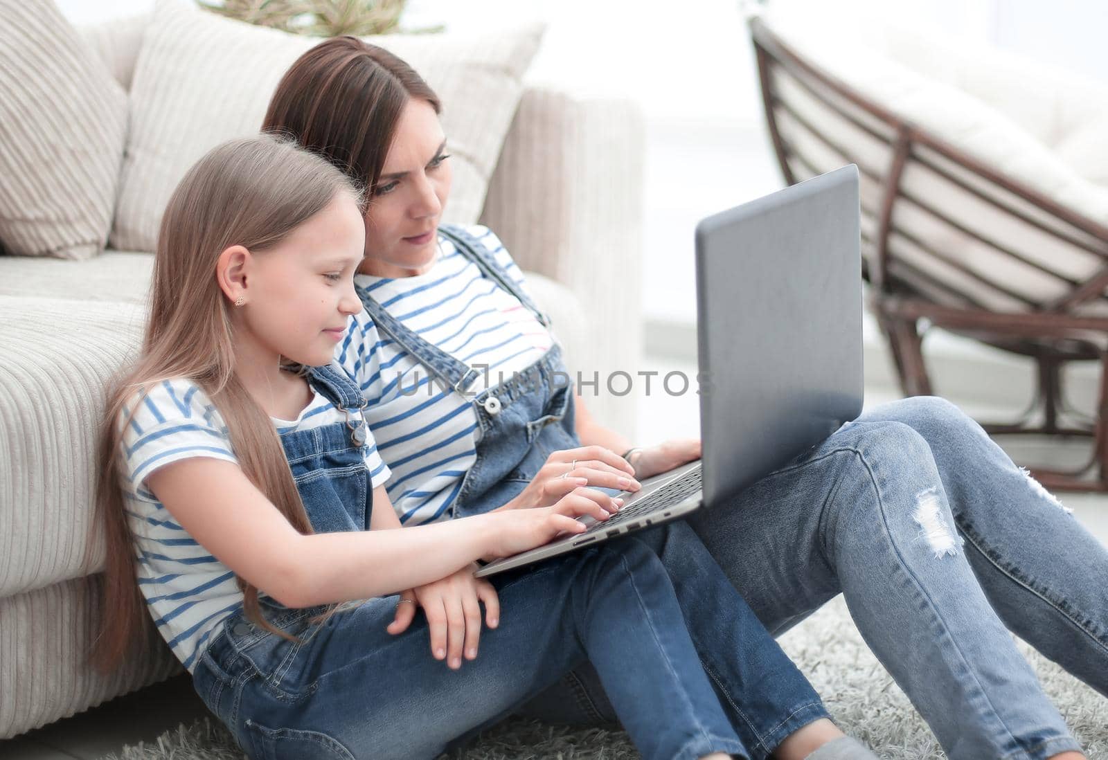 mom and daughter sitting on the carpet in the living room and using a laptop.photo with copy space