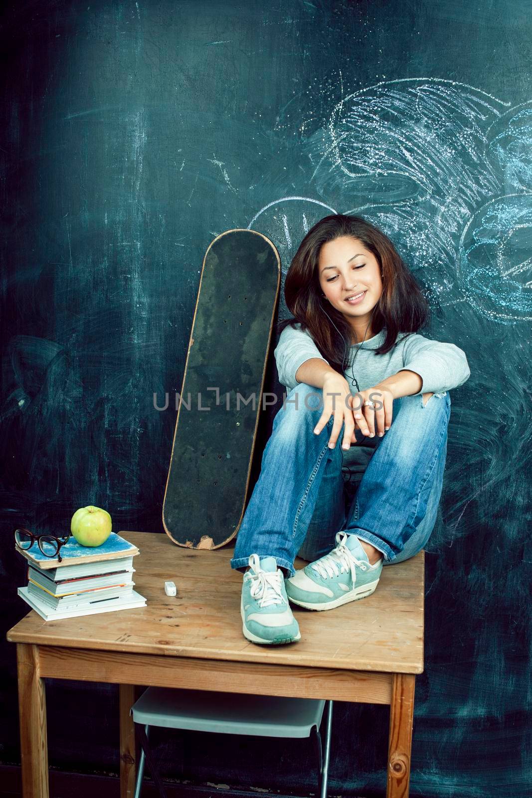 young cute teenage girl in classroom at blackboard seating on table smiling, modern hipster concept closeup