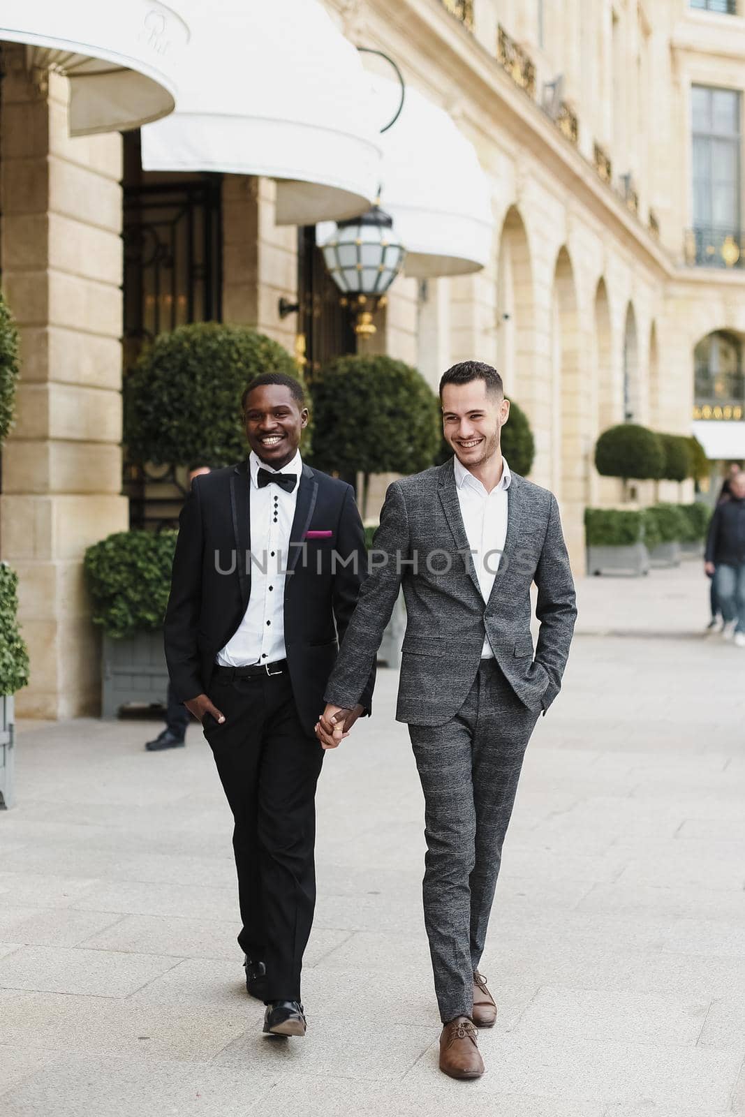 Afro american and caucasian happy handsome gays walking outside and holding hands in city. Concept of same sex male couple.