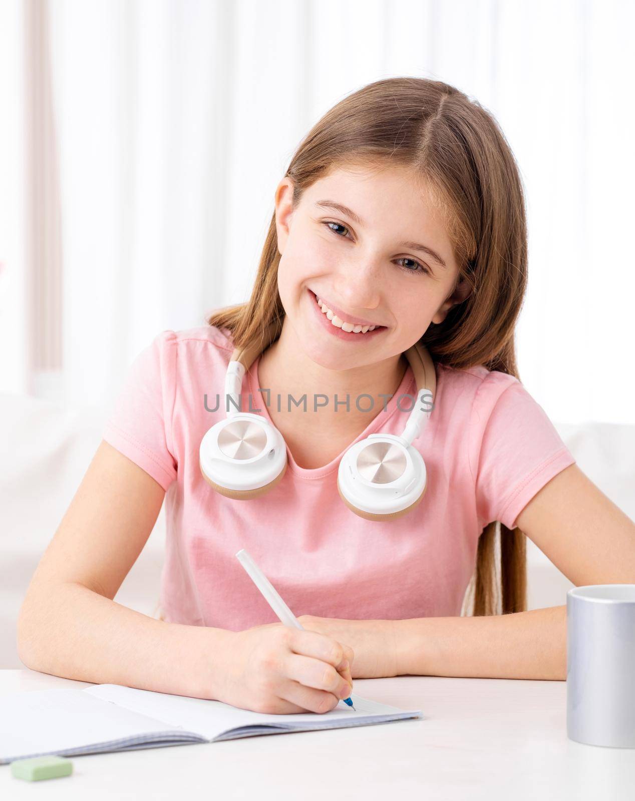 Pretty school girl making homework with listening to online lessons on headphones
