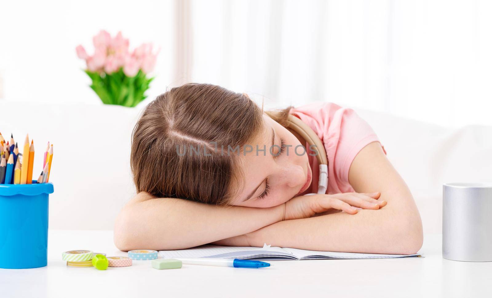 Cute lovely schoolgirl is tired and sleeps on desk indoors