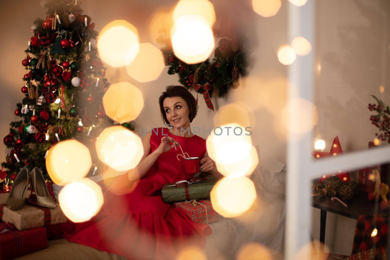 Beautiful caucasian female in red dress looks at the box with Christmas gift and drinks hot tea