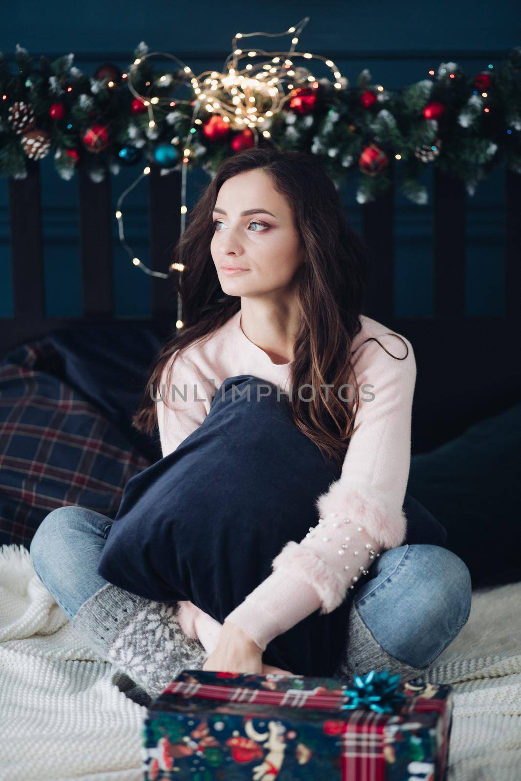 Beautiful young woman with long hair sits on a bed and thinks about something by StudioLucky