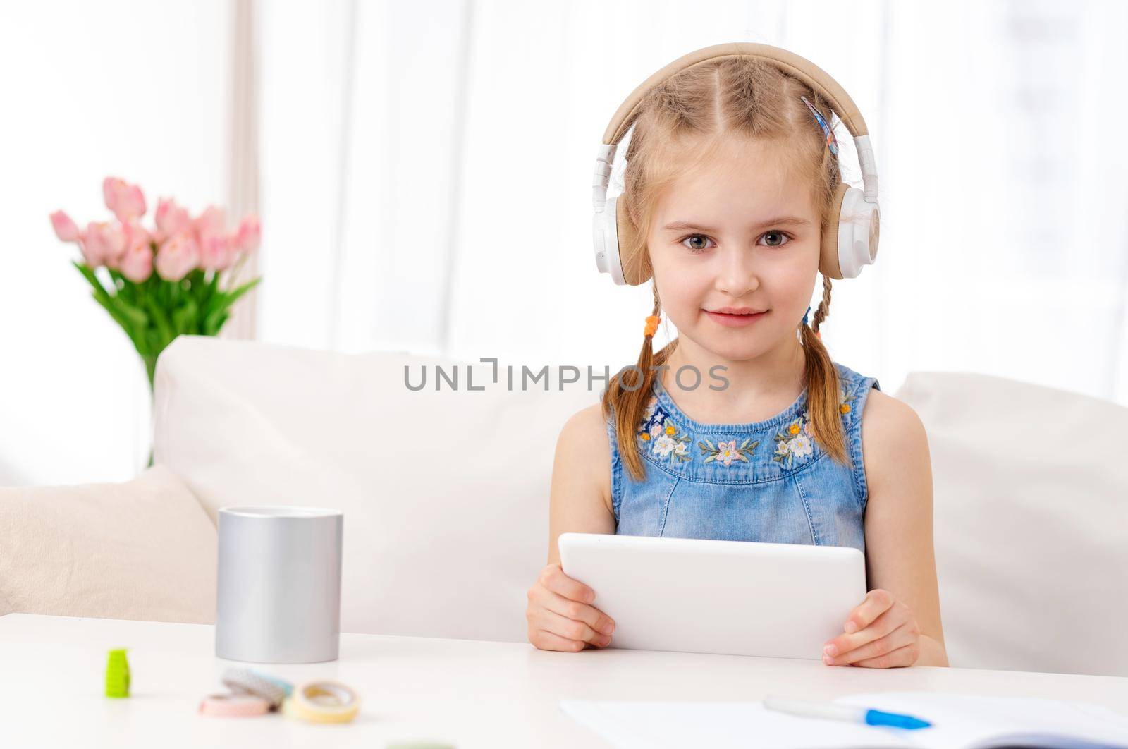Beatiful little girl with white tablet with headphones on, in the room