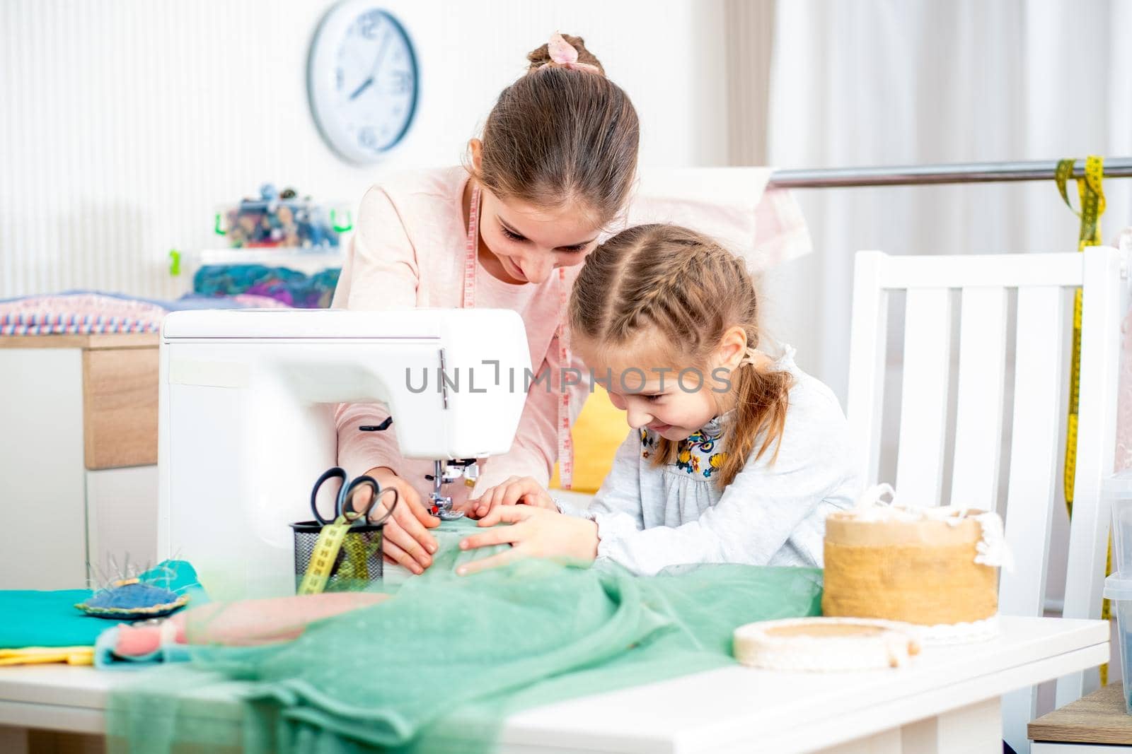 Smiling happy sister teaches a little girl to sew on a sewing machine by herself