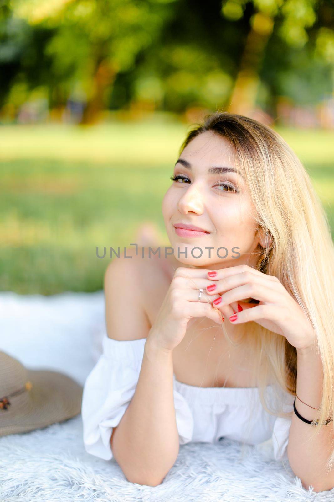 Young girl with red nails lying in park on plaid. Concept of having free time, picnic and summer vacations.