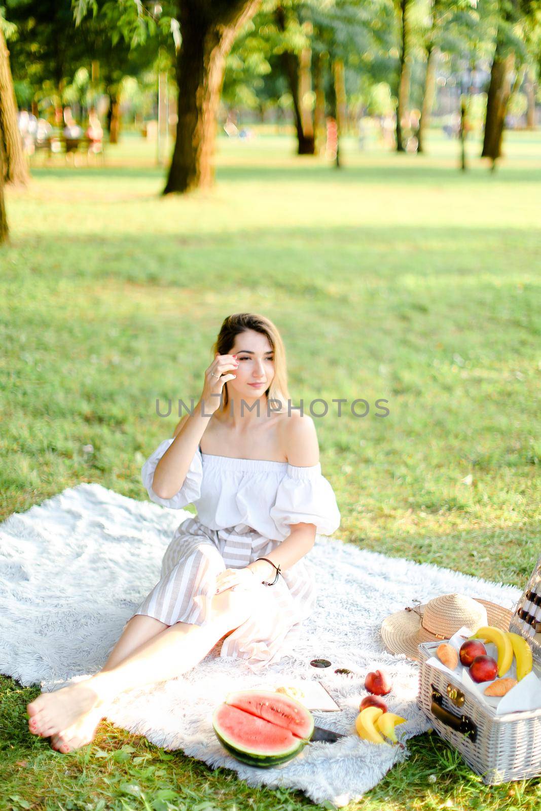 Young woman having picnic on plaid and sitting in park with fruits. by sisterspro