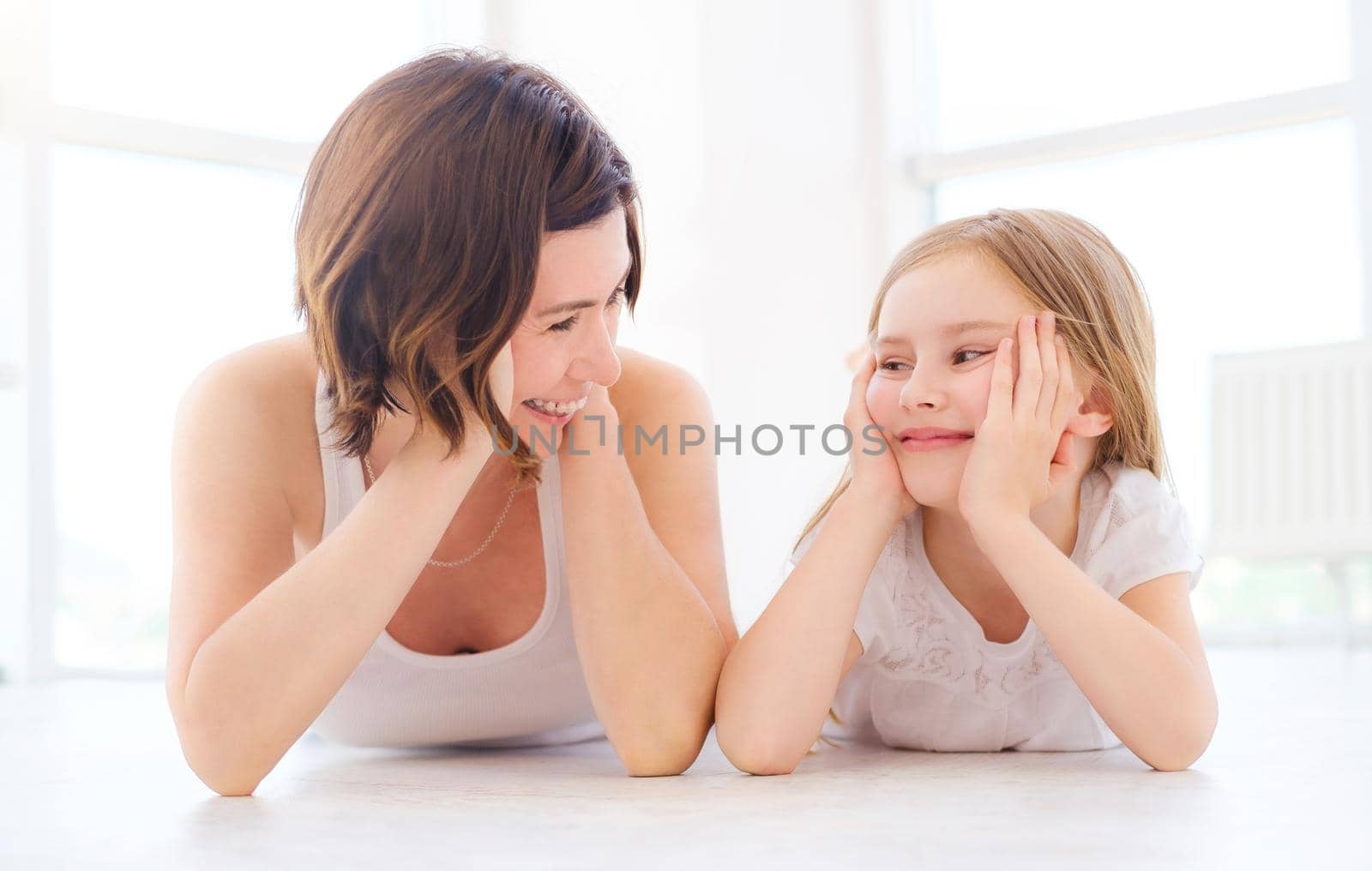 Mother with her little daughter girl luing on a floor in light room