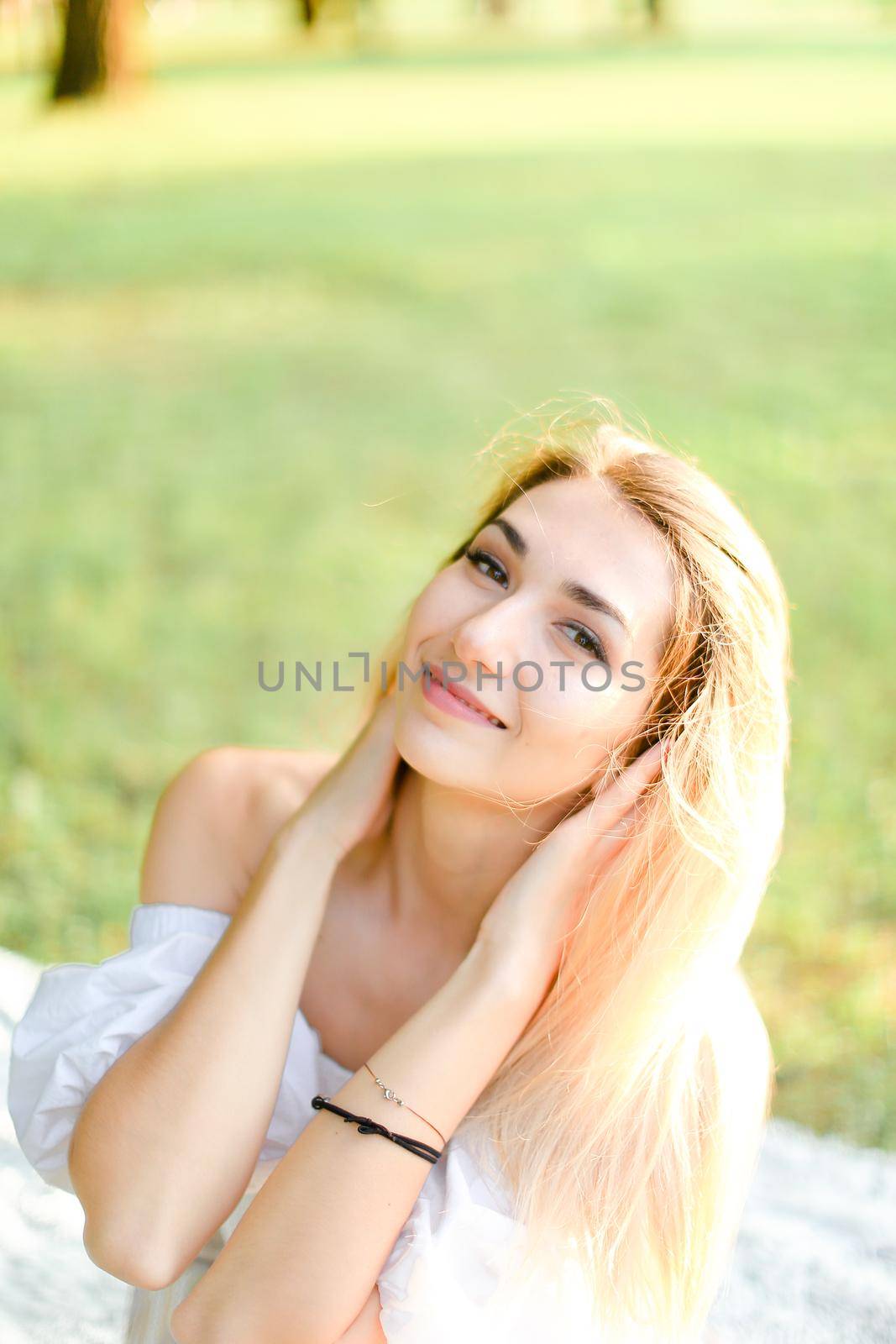 Portrait of young blonde happy girl sitting on plaid, grass in background. by sisterspro