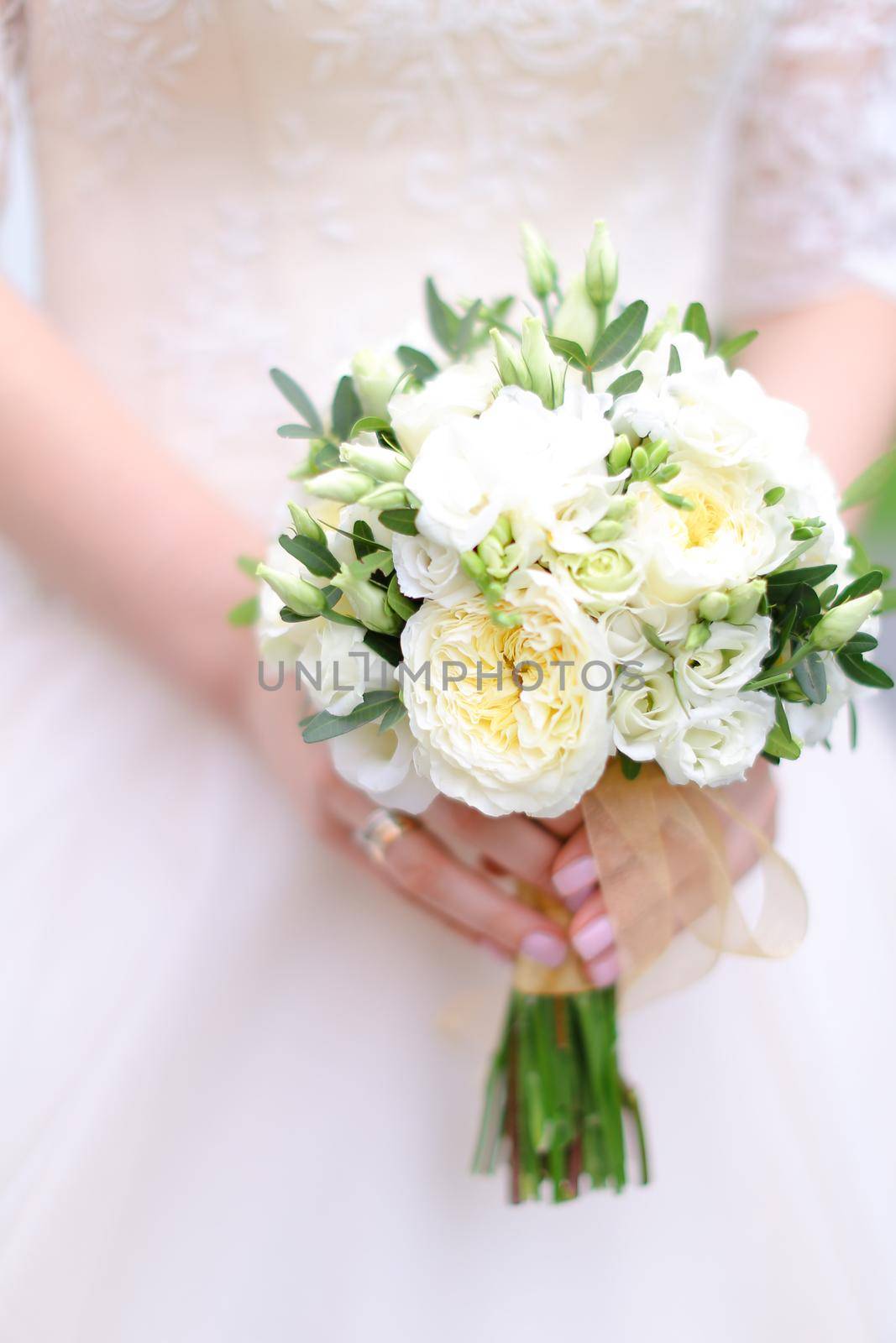Closeup bride hands keeping white bouquet of flowers. Concept of wedding photo session.