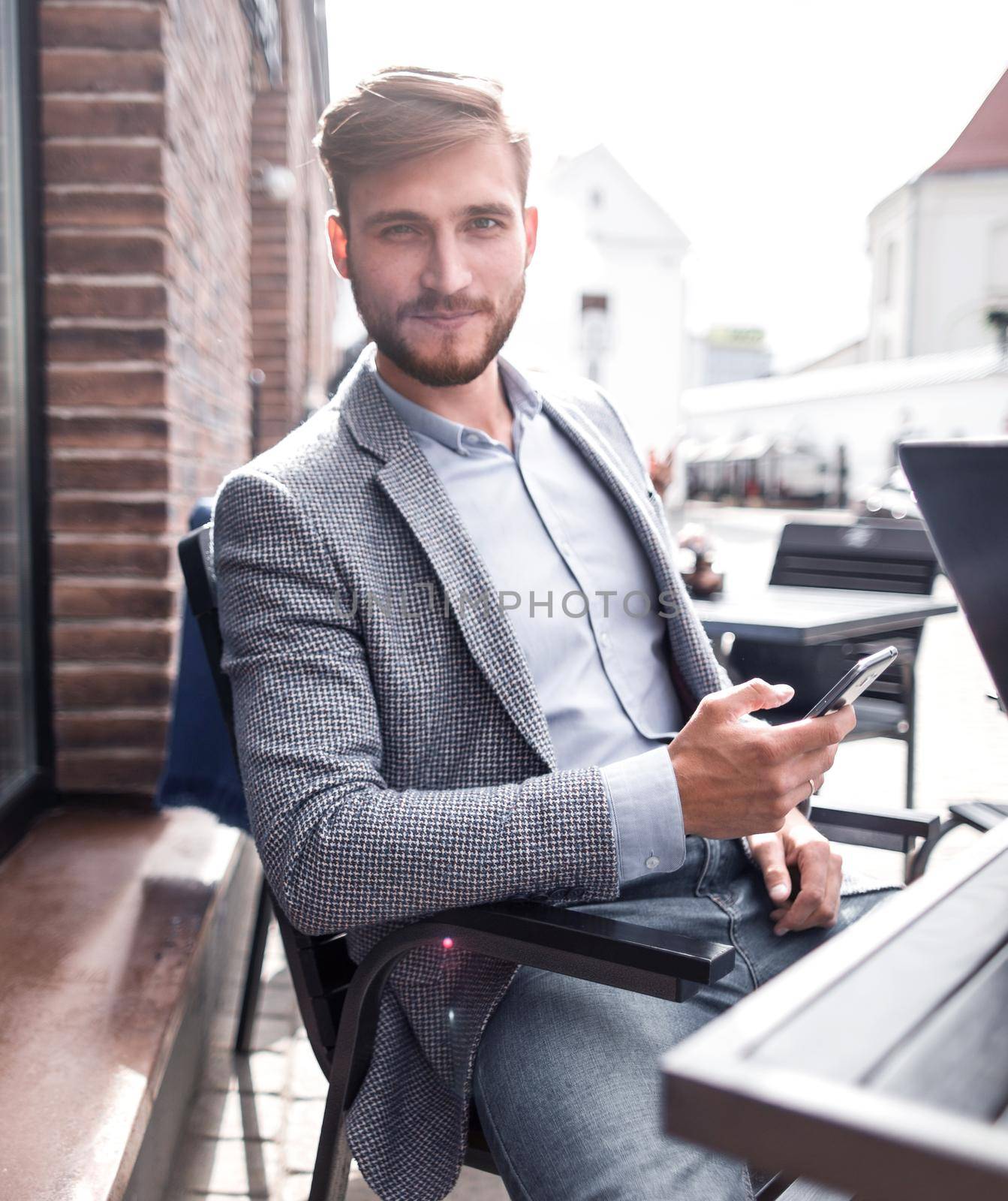businessman with a smartphone sitting at a table in a street cafe by asdf