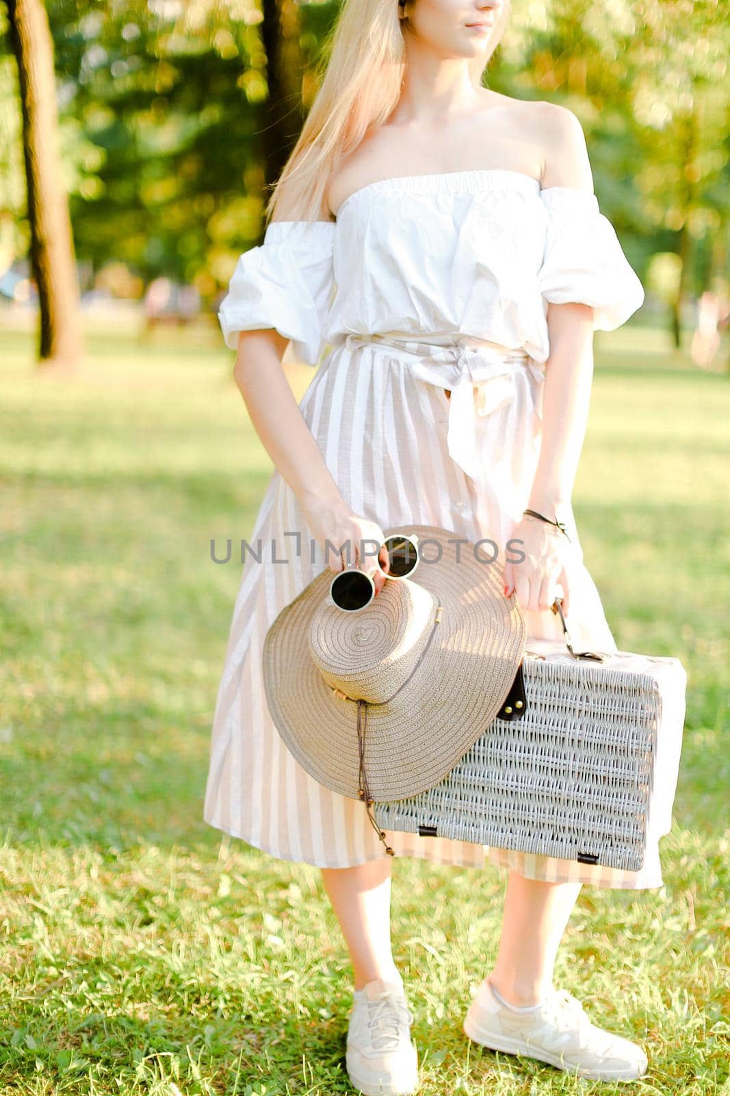 Caucasian female person standing with sunglasses and bag in garden. Concept of summer fashion and walking in park.