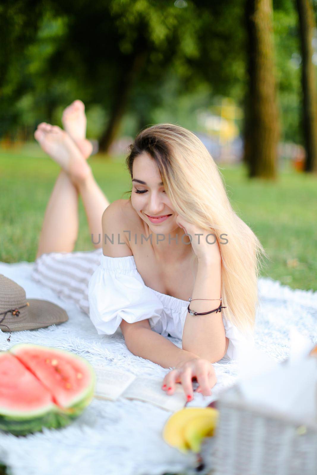 Young happy woman lying on plaid in park and reading book. by sisterspro