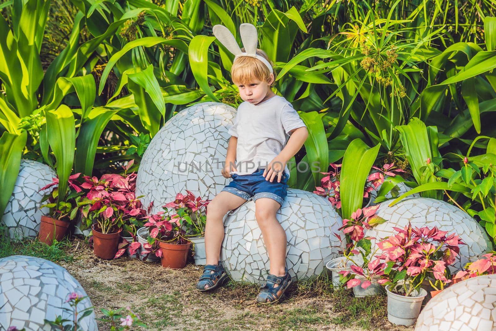 Cute little kid boy with bunny ears having fun with traditional Easter eggs hunt, outdoors. Celebrating Easter holiday. Toddler finding, colorful eggs.