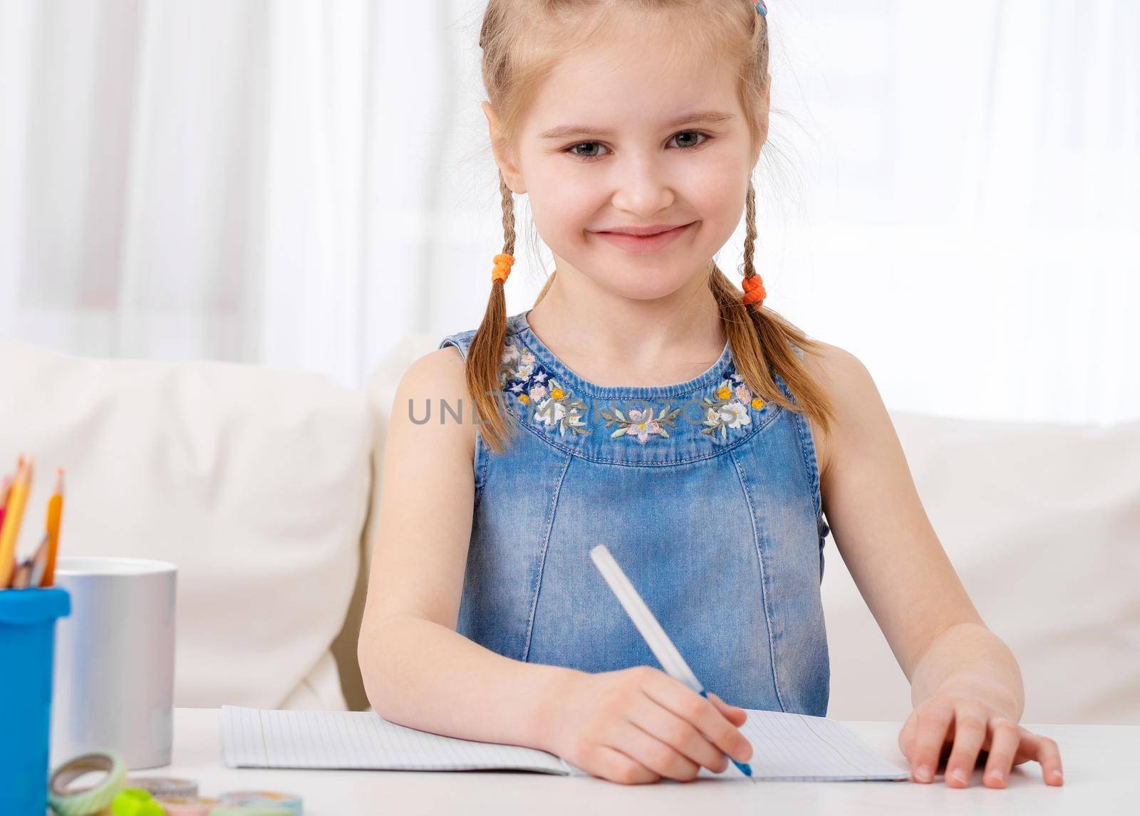 Smiling happy young girl sitting at desk and doing his homework.