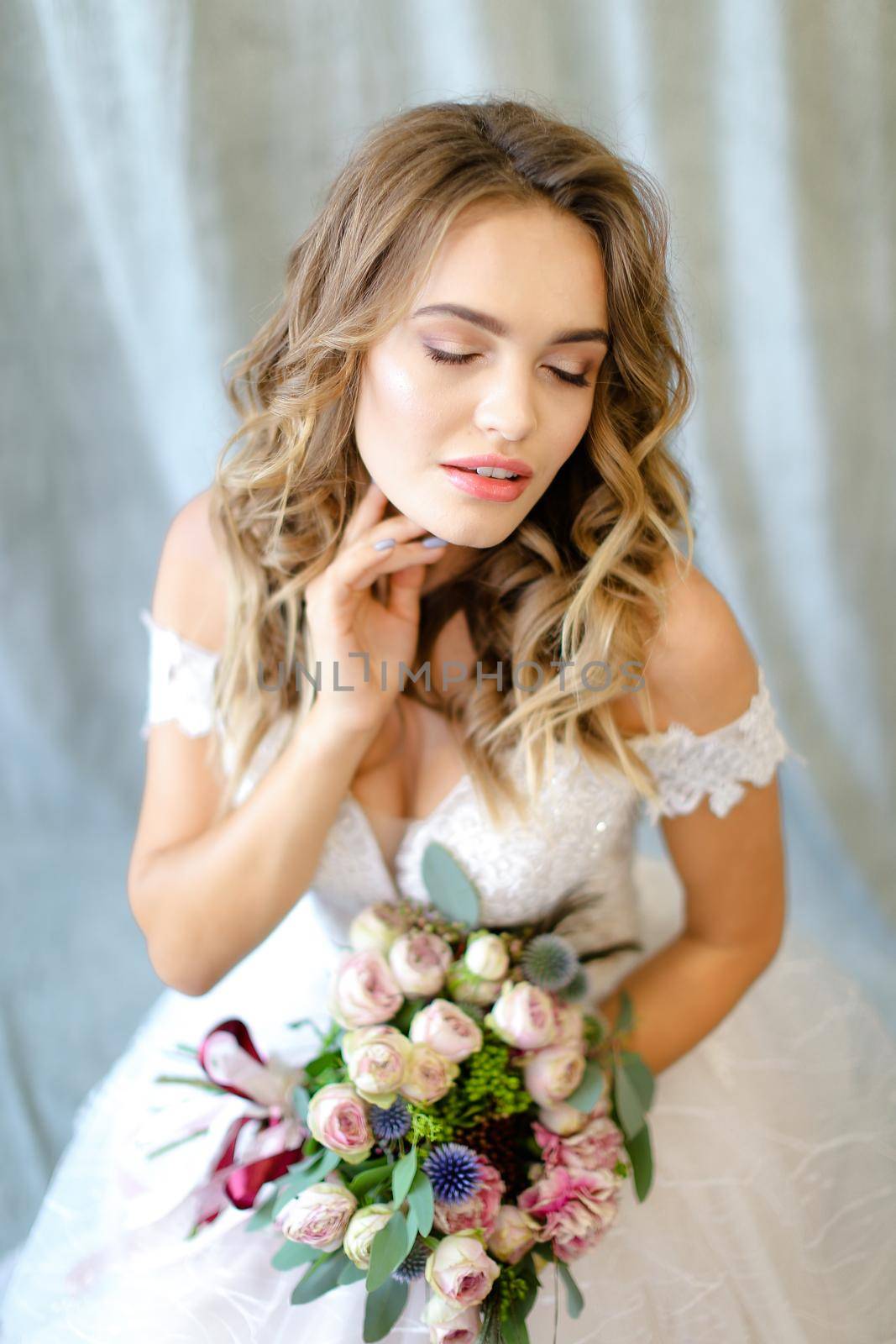 Young charming bride wearing white dress with bouquet at photo studio. Concept of bridal photo session, wedding and floristic art.